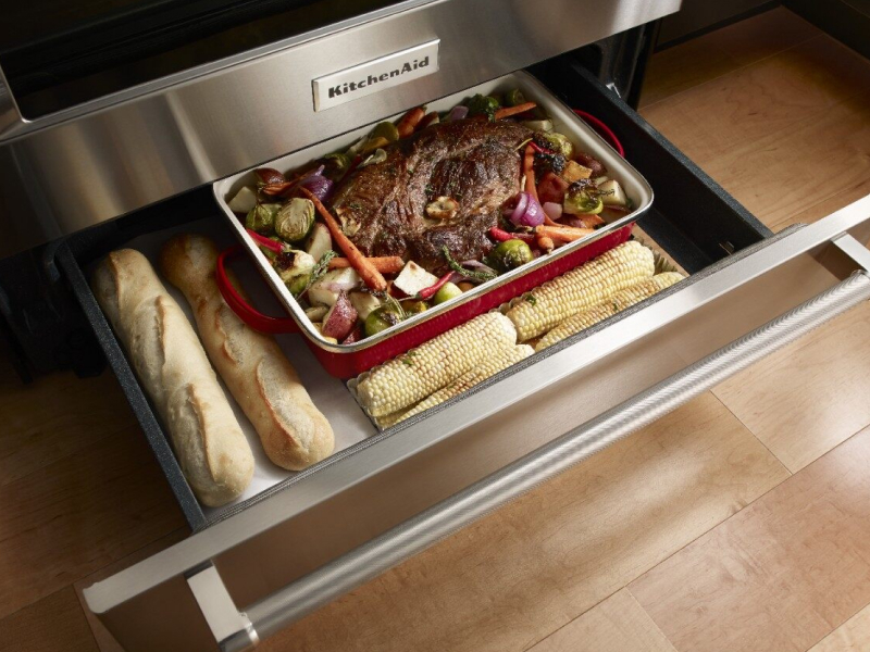 Open warming drawer with bread, a roast and vegetables inside