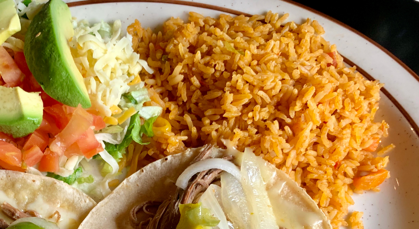 Seasoned rice on a plate with tacos and avocado