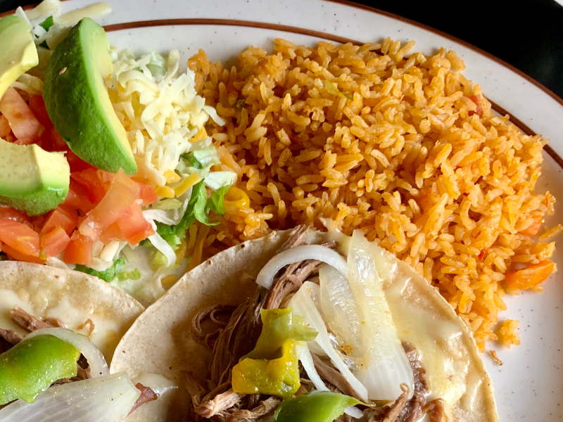Seasoned rice on a plate with tacos and avocado