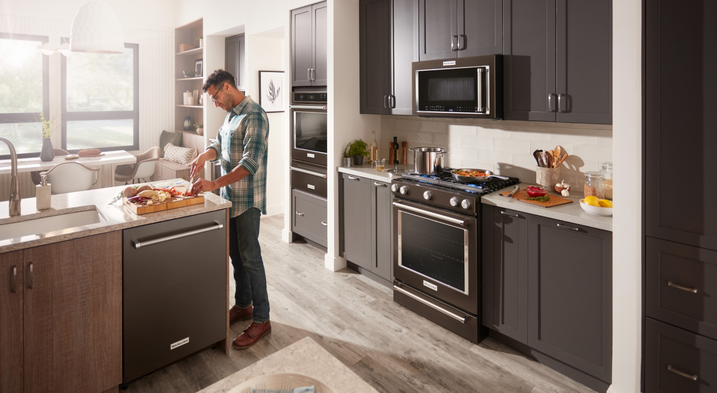 A man chopping ingredients in front of a KitchenAid® slide-in range and microwave