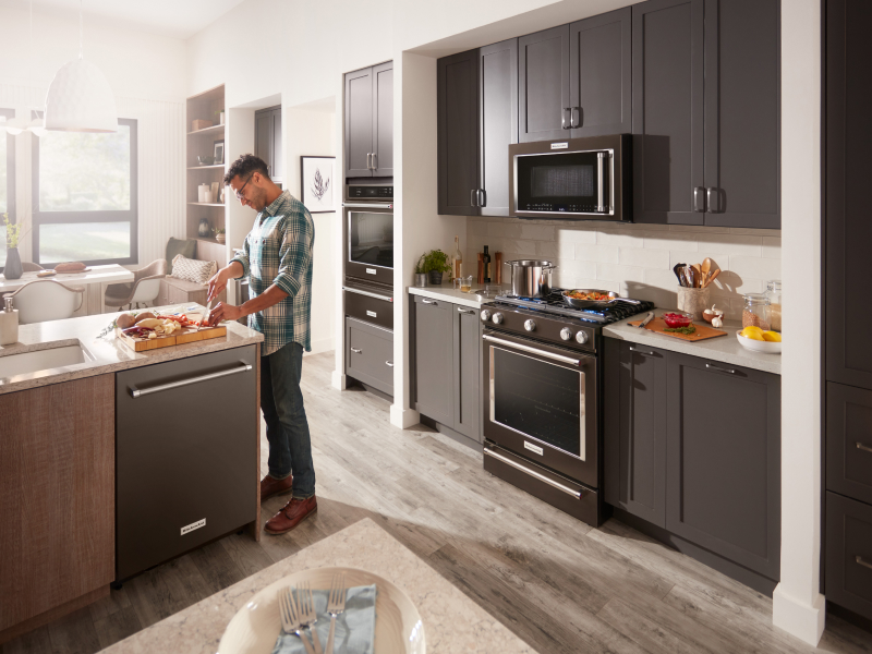 A man chopping ingredients in front of a KitchenAid® slide-in range and microwave