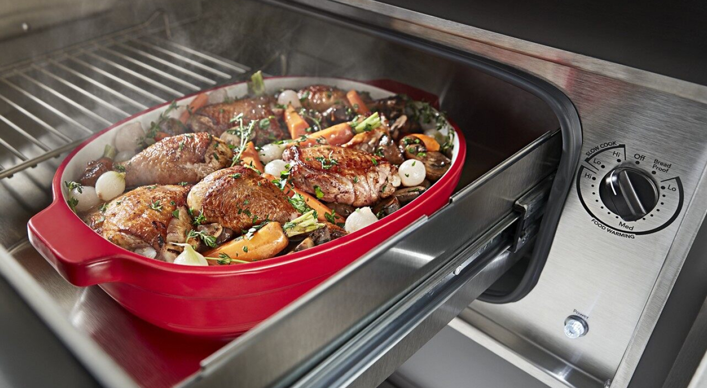  Roasted chicken thighs and vegetables in a casserole dish inside of a warming drawer