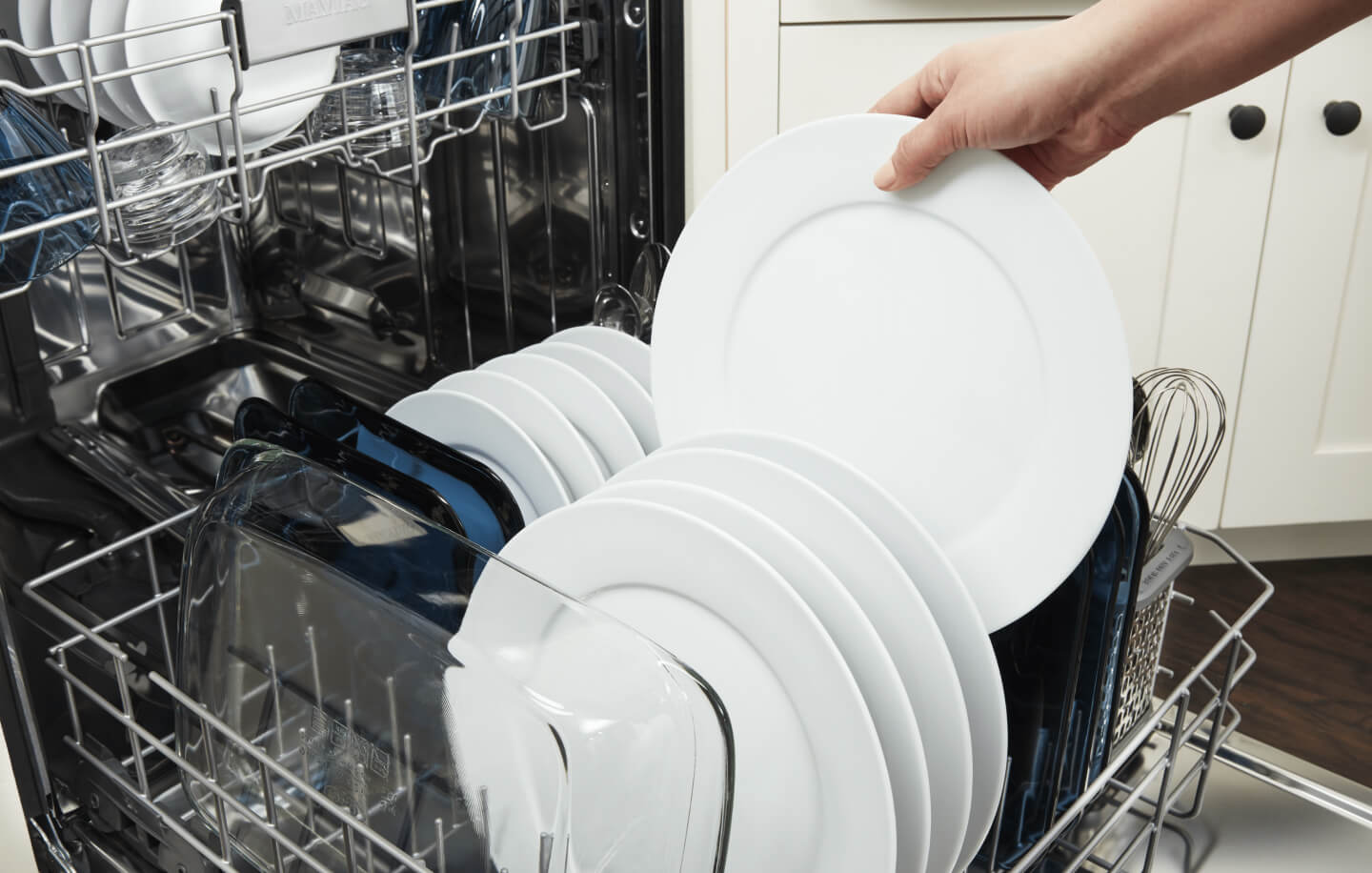 Person placing a white dish into a dishwasher