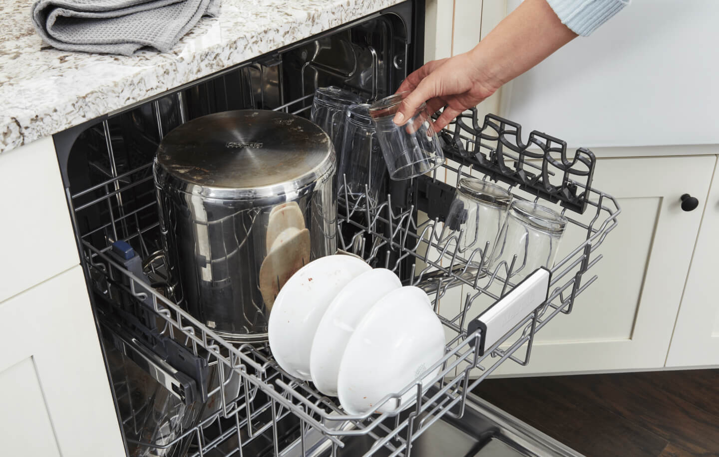 Person placing a glass cup into a dishwasher
