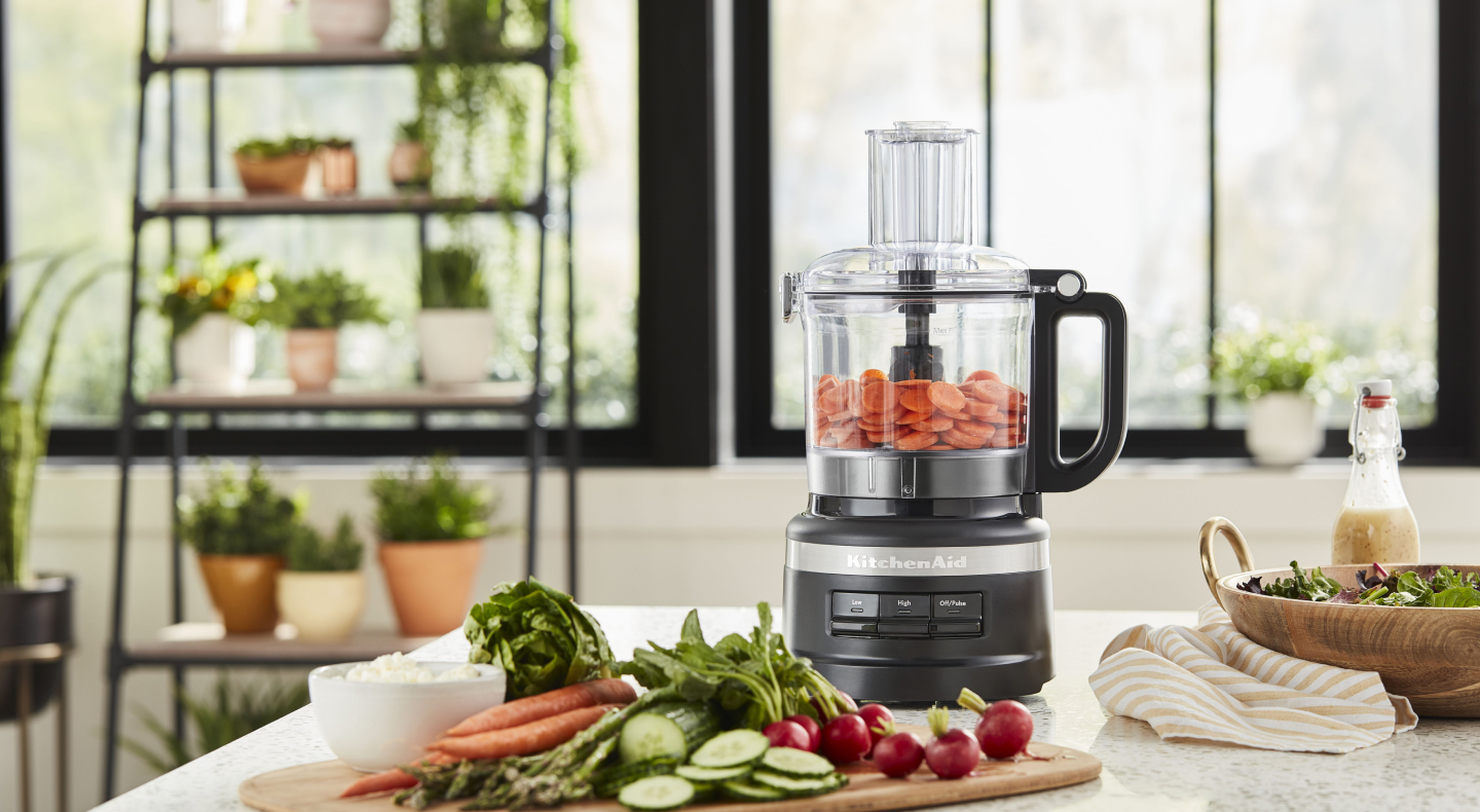 A food processor and cutting board with charcuterie ingredients
