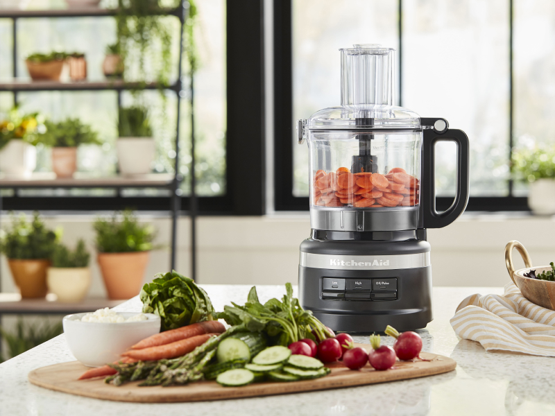 A food processor and cutting board with charcuterie ingredients
