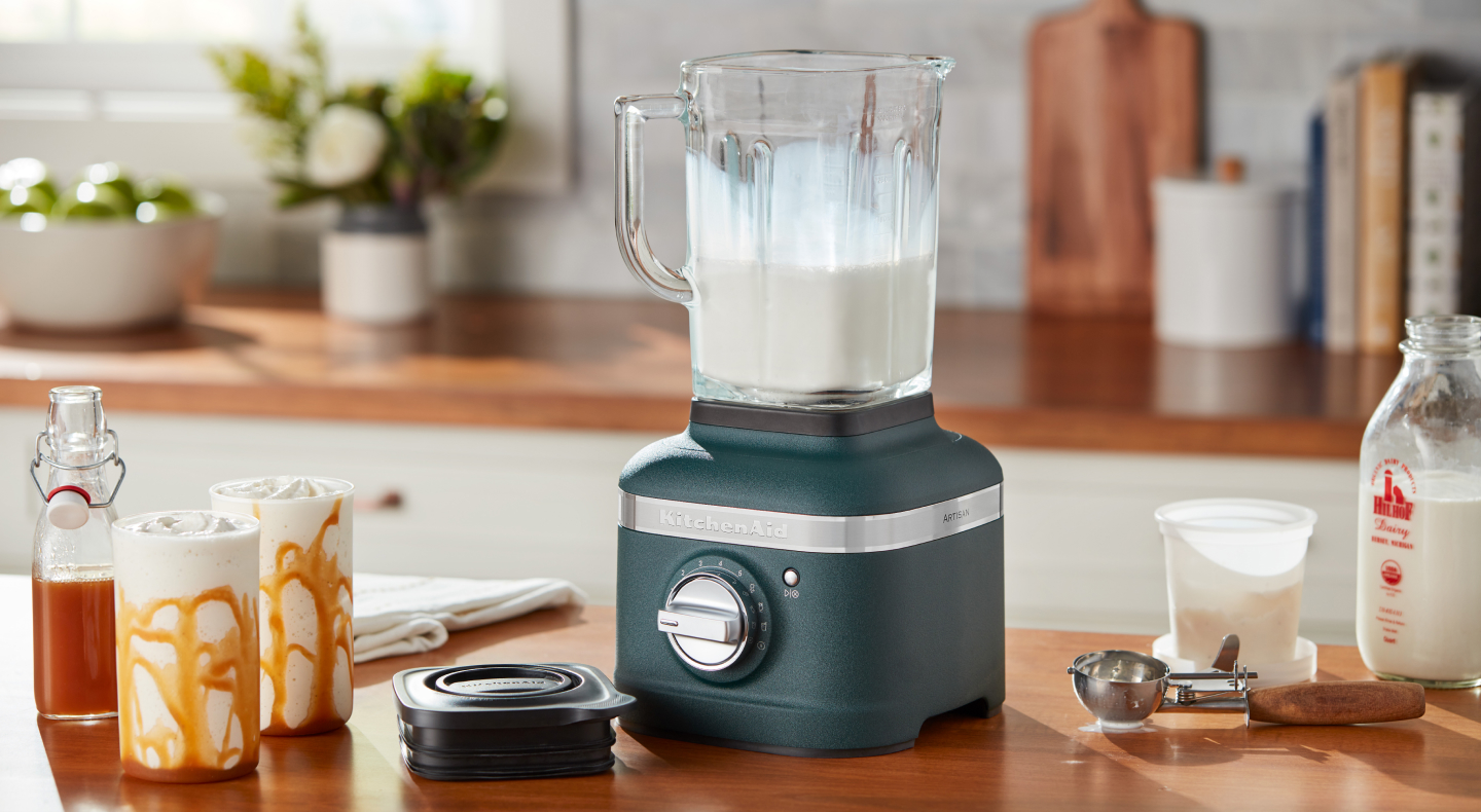 Blue blender filled with vanilla milkshake mixture next to milkshakes with caramel