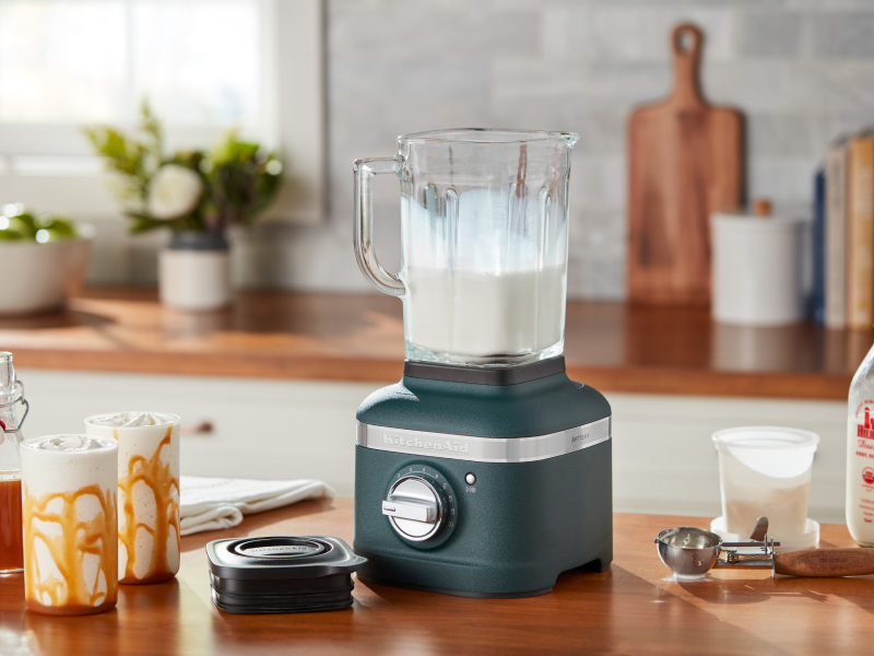 Blue blender filled with vanilla milkshake mixture next to milkshakes with caramel