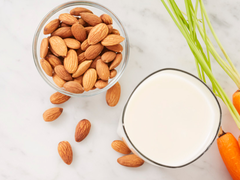 Carrots next to a bowl of almonds and glass of milk