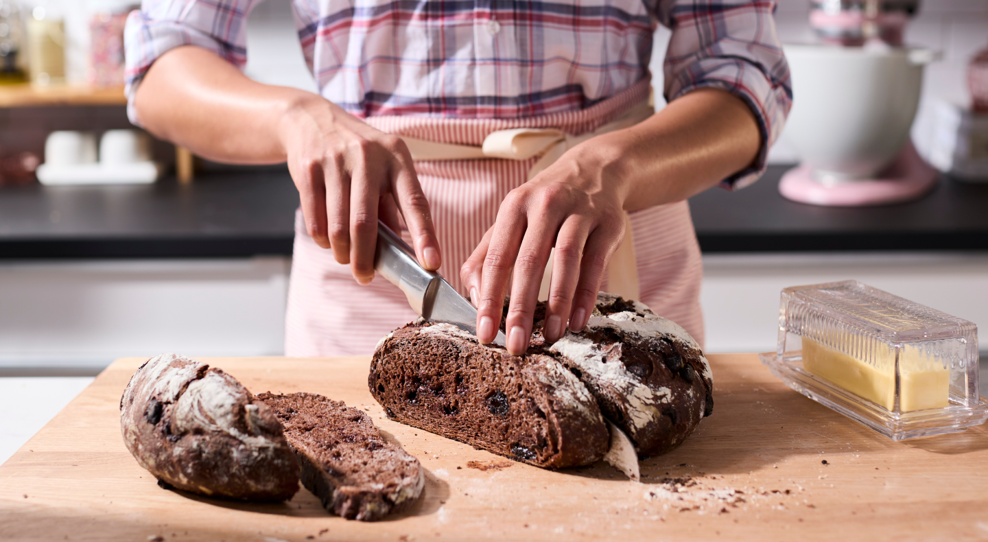 Person slicing a loaf of bread on a wooden cutting board