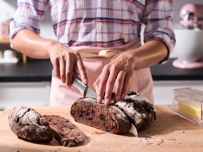 Person slicing a loaf of bread on a wooden cutting board