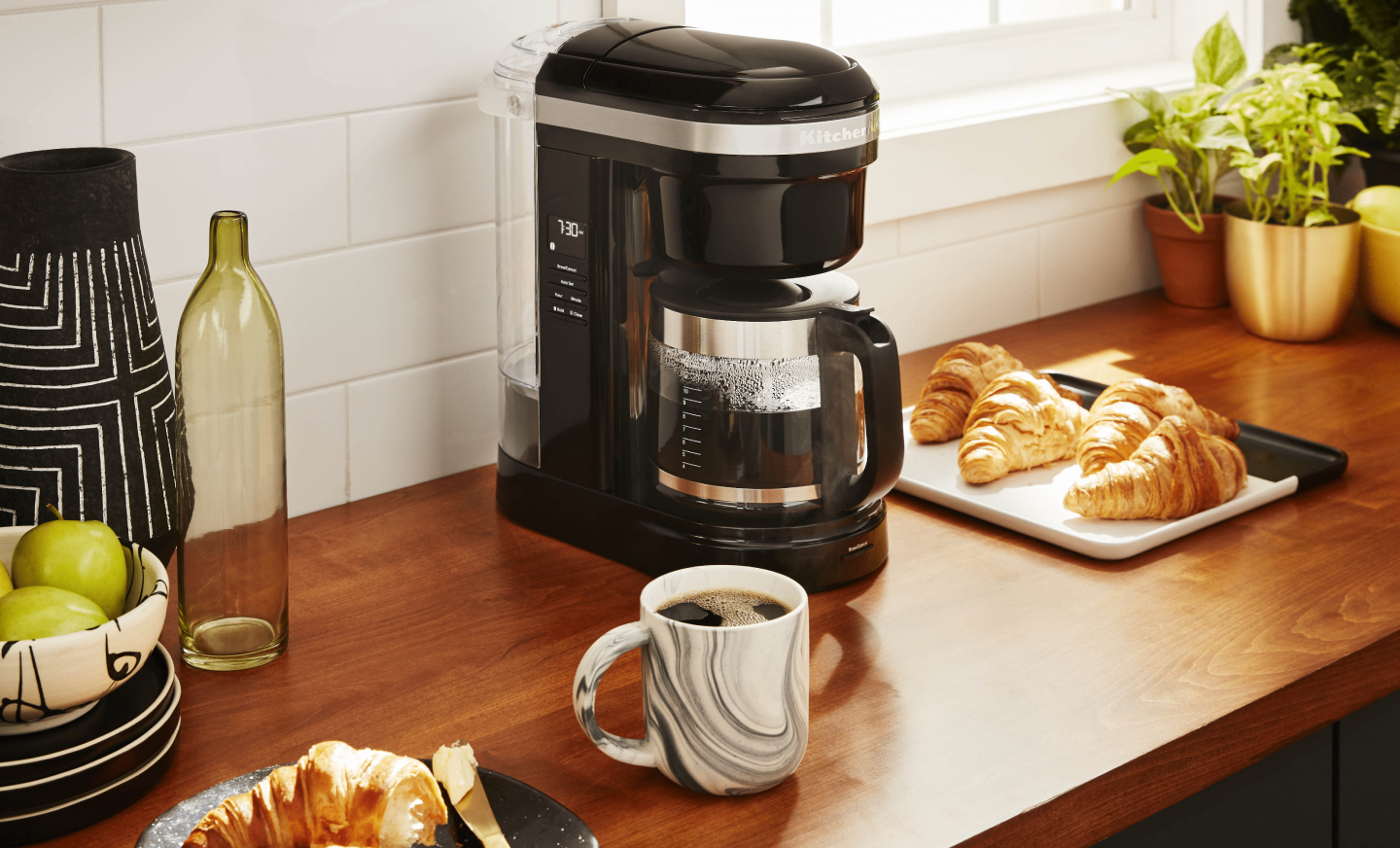 KitchenAid® coffee maker on countertop with croissants and mug of coffee