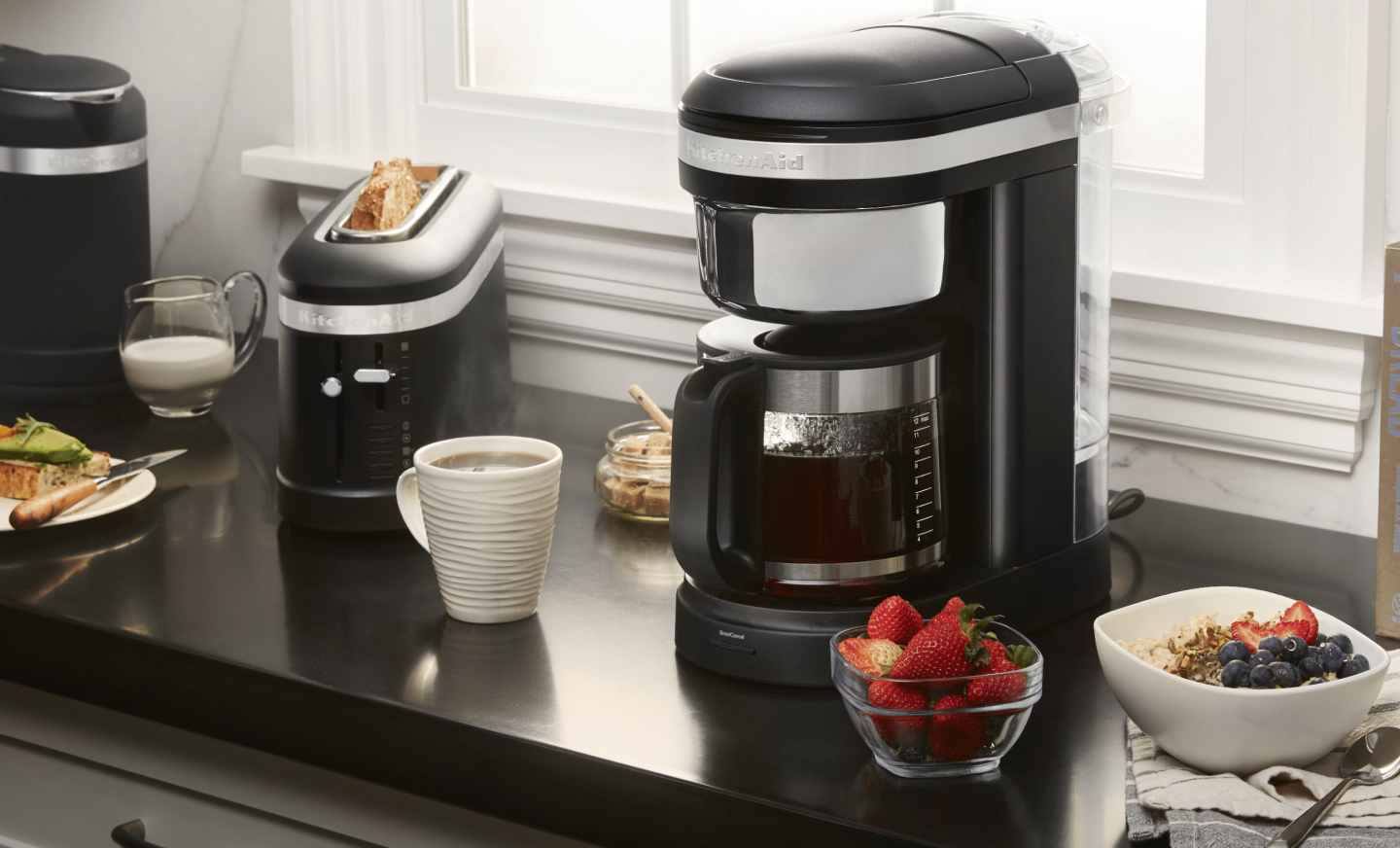 KitchenAid® coffee maker on countertop with coffee drink and breakfast foods