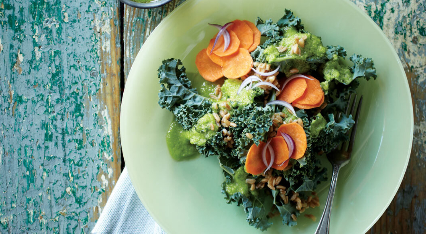 A closeup of a chopped kale salad with sliced carrots and onions.