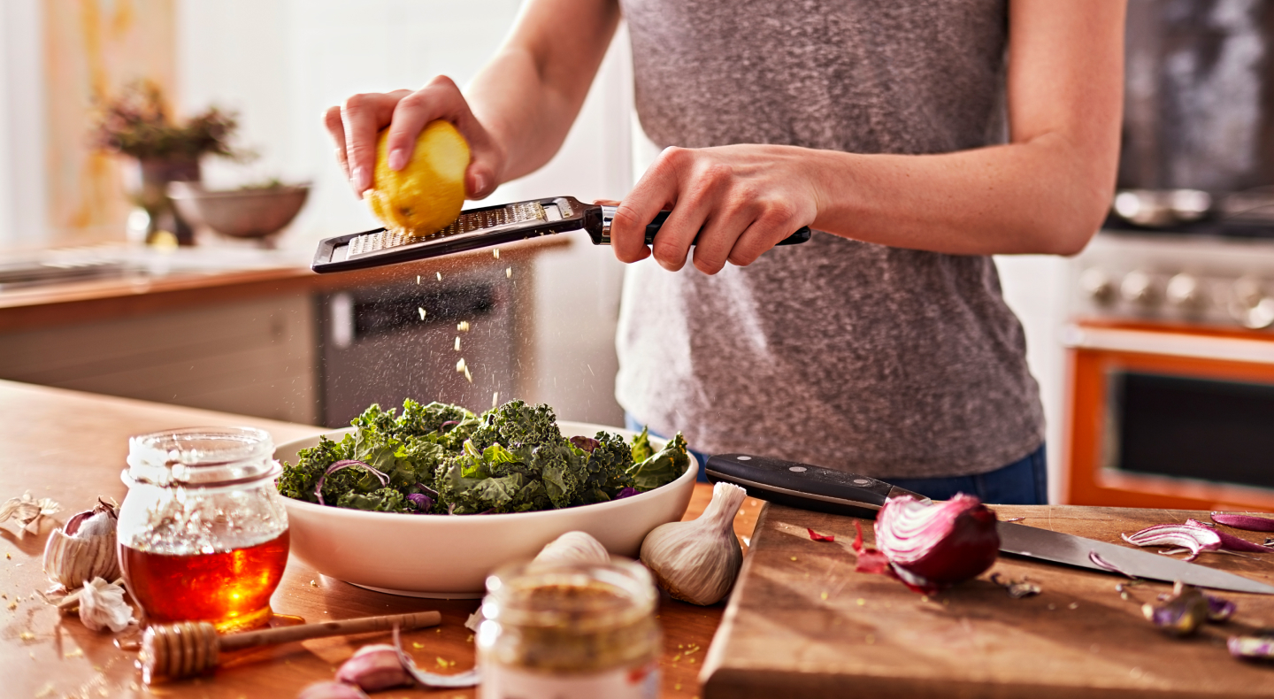 A woman shredding lemon peel onto a chopped salad in a modern kitchen.