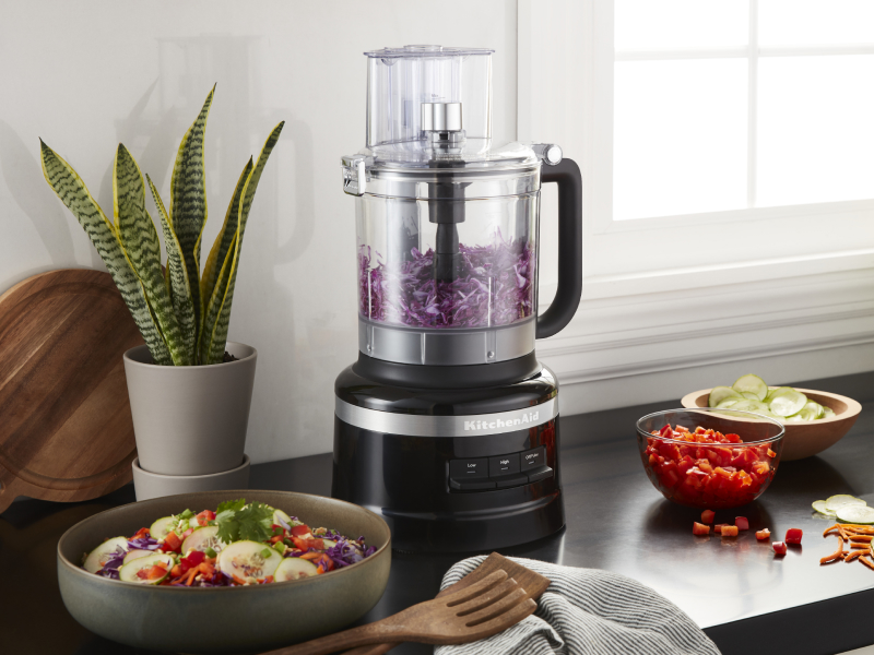 KitchenAid® food processor with purple cabbage next to a chopped salad and the ingredients in a modern kitchen.
