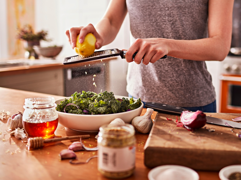 A woman shredding lemon peel onto a chopped salad in a modern kitchen.