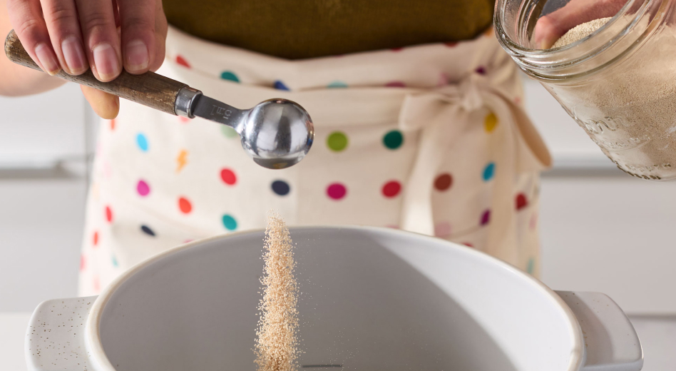 Person adding cinnamon roll bread ingredients into a bowl