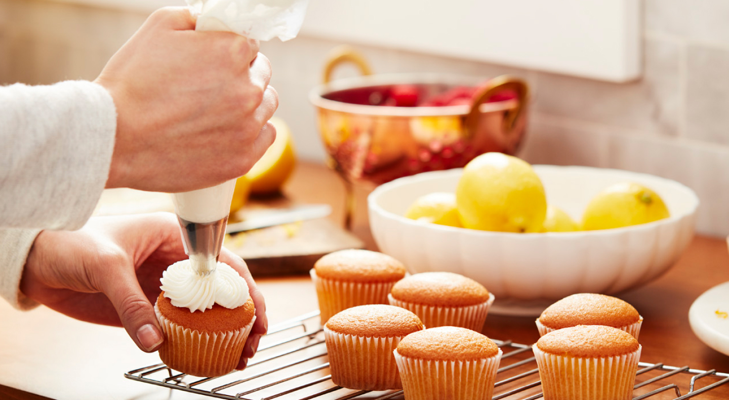 Vanilla cupcakes being frosted with cream cheese frosting