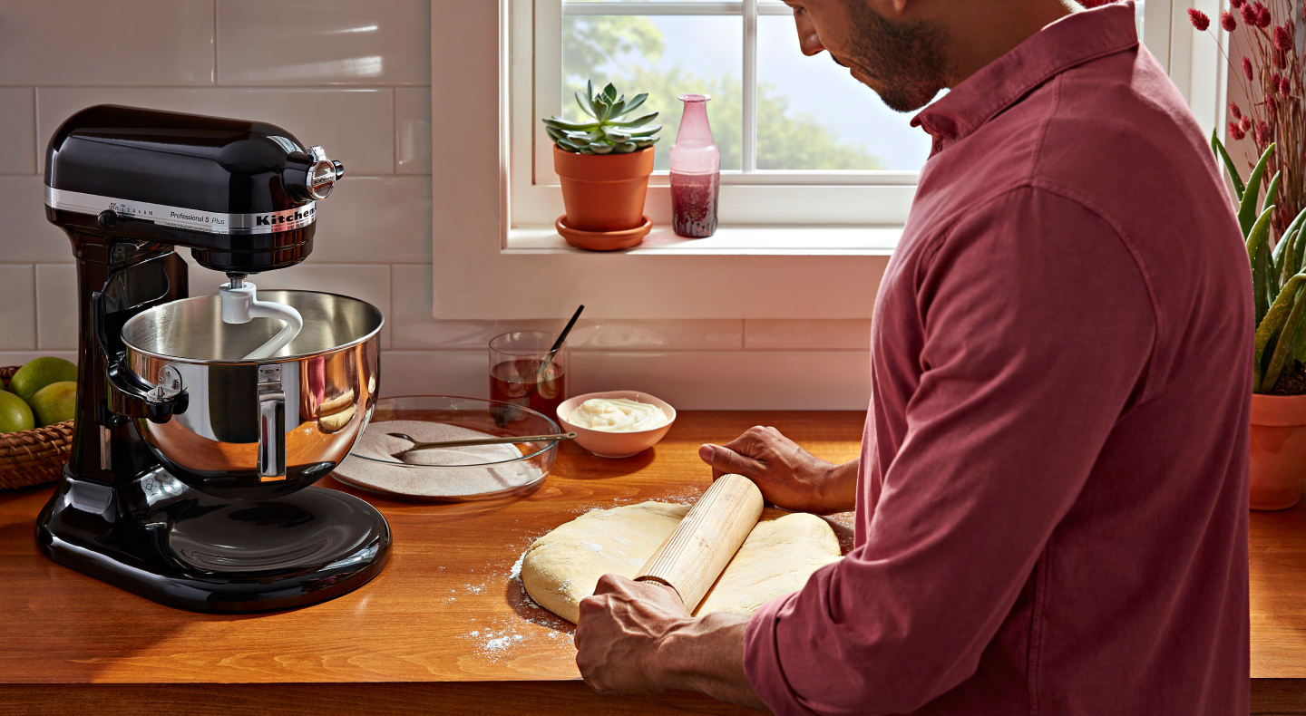 Person rolling out dough next to a black KitchenAid® stand mixer