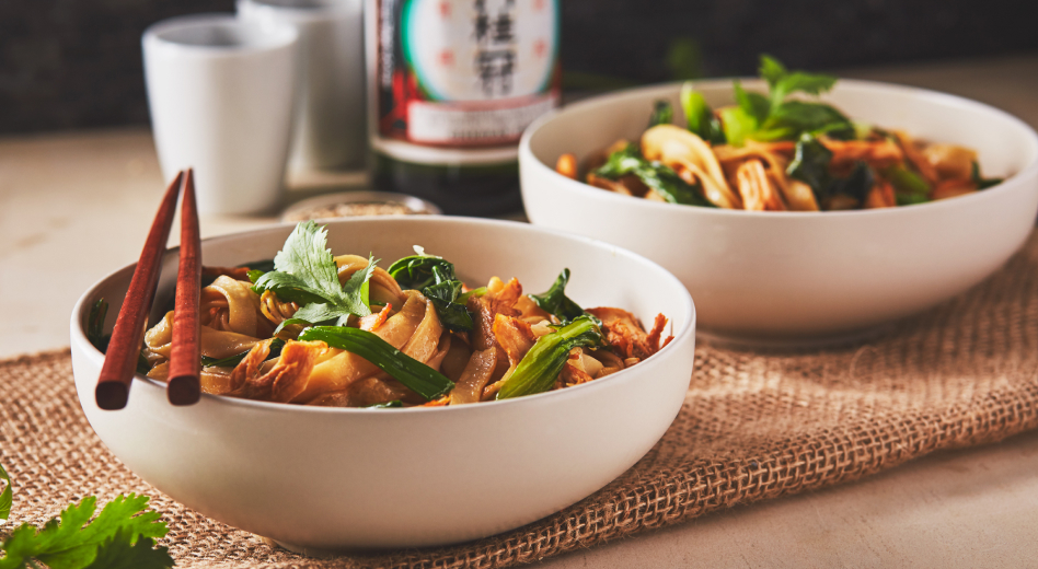 Two bowls of fettuccine noodles on a table with wooden chopsticks