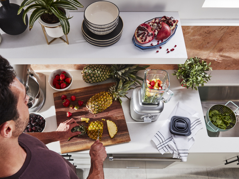 Person cutting pineapple next to KitchenAid® blender with fruit in it