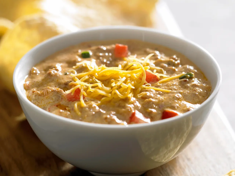 Close-up of bowl of queso with cheese sprinkled on top and mixed-in veggies