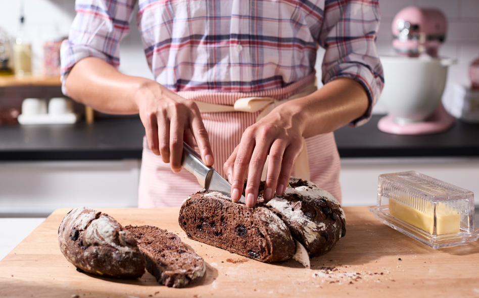 Maker using knife to cut slice of rye bread on cutting board