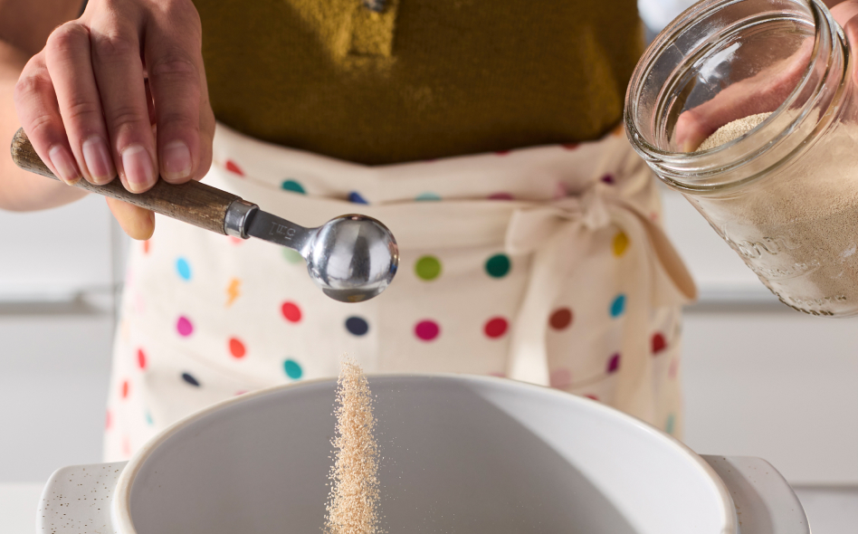 Maker tipping spoon full of yeast into a bread bowl