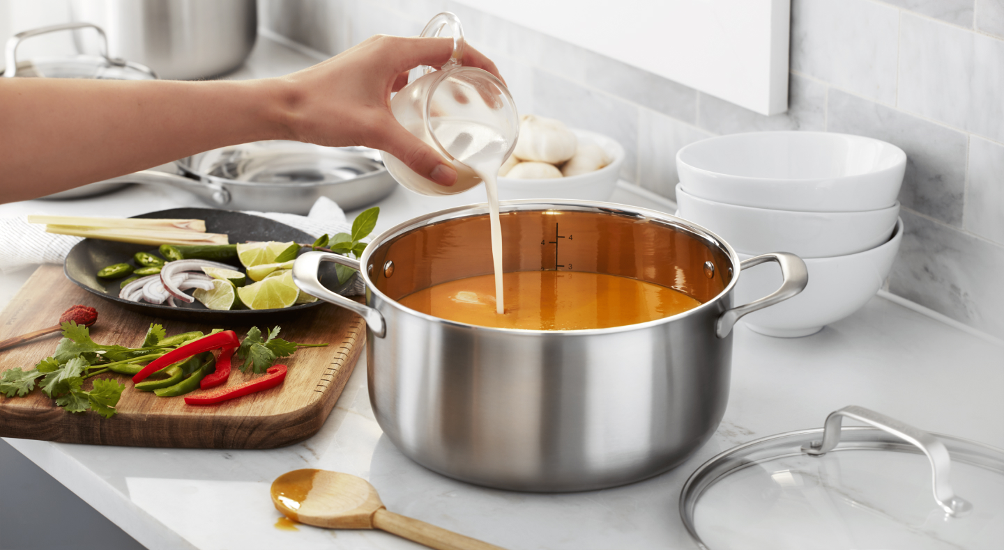 Person pouring cream into pot of soup