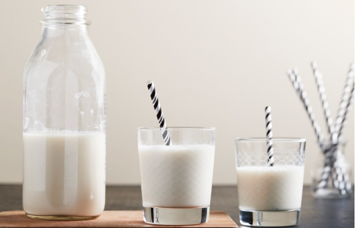 Two glasses of milk with black and white paper straws sitting on counter next to milk bottle