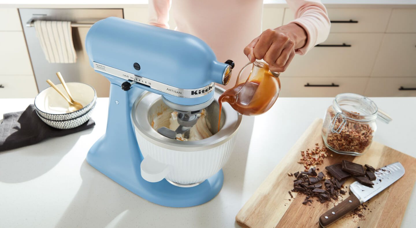 Hand pouring caramel into a KitchenAid® stand mixer bowl with ice cream inside