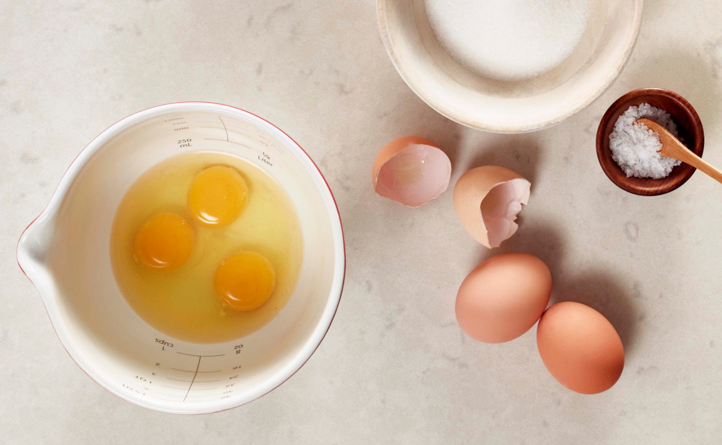 Three eggs in a bowl next to cracked egg shells
