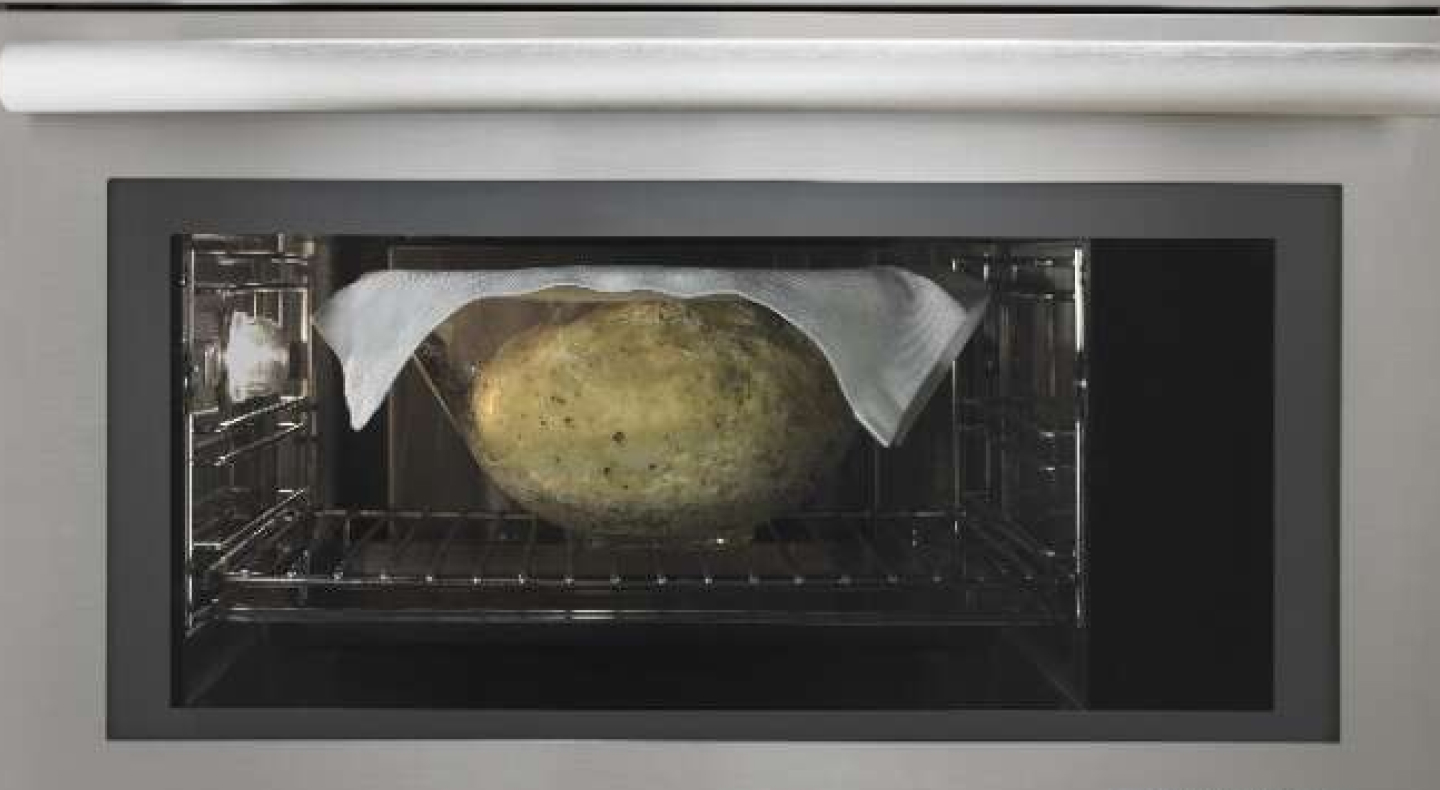 Bread rising in a glass bowl, with a cloth on top, inside of a convection microwave