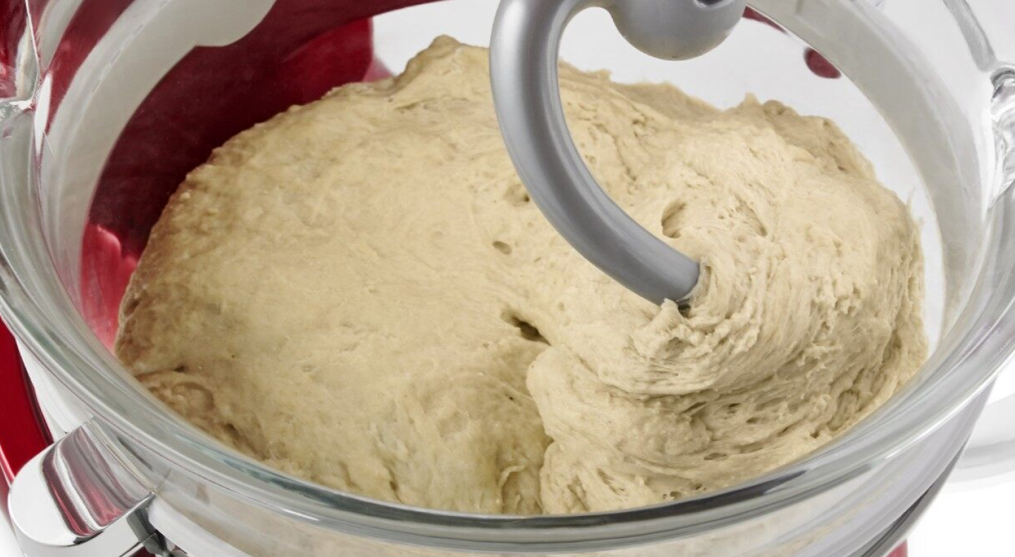 Close-up of a dough hook inside of bread dough in a stand mixer bowl
