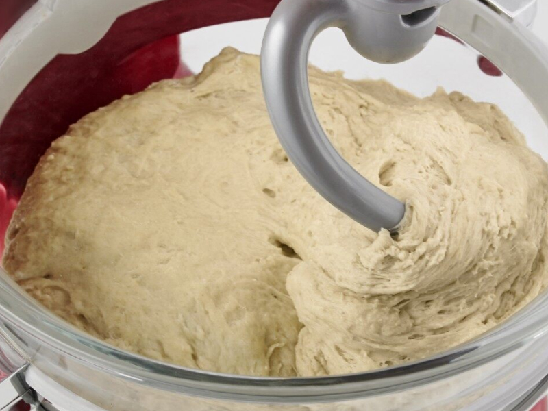 Close-up of a dough hook inside of bread dough in a stand mixer bowl