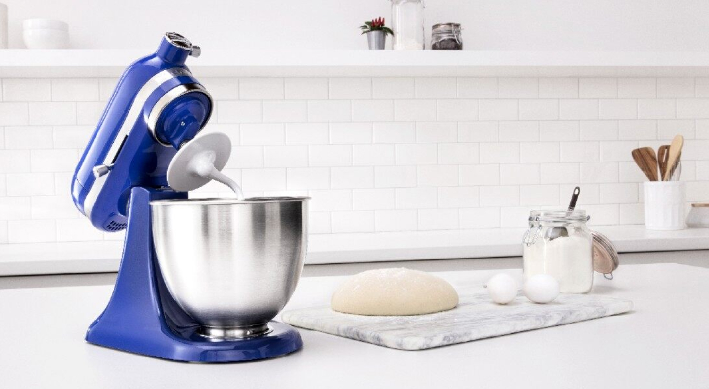 Blue KitchenAid® stand mixer next to a cutting board with bread dough and ingredients