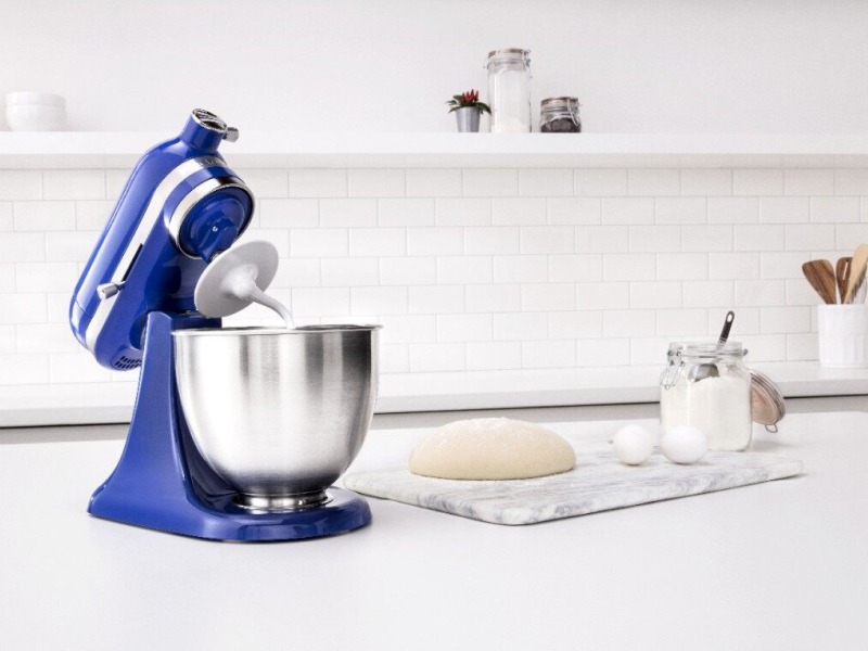 Blue KitchenAid® stand mixer next to a cutting board with bread dough and ingredients