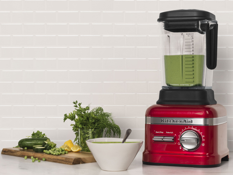 Red KitchenAid® blender next to various vegetables