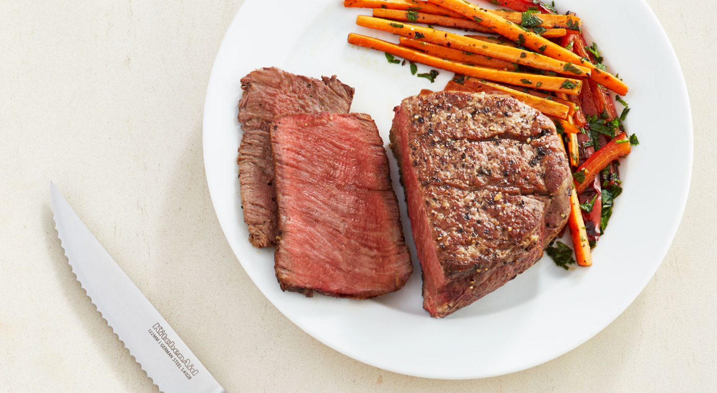 A half cut seasoned steak dish with carrots on the side