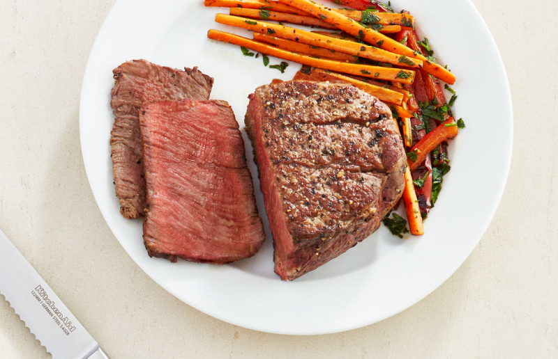 A half cut seasoned steak dish with carrots on the side