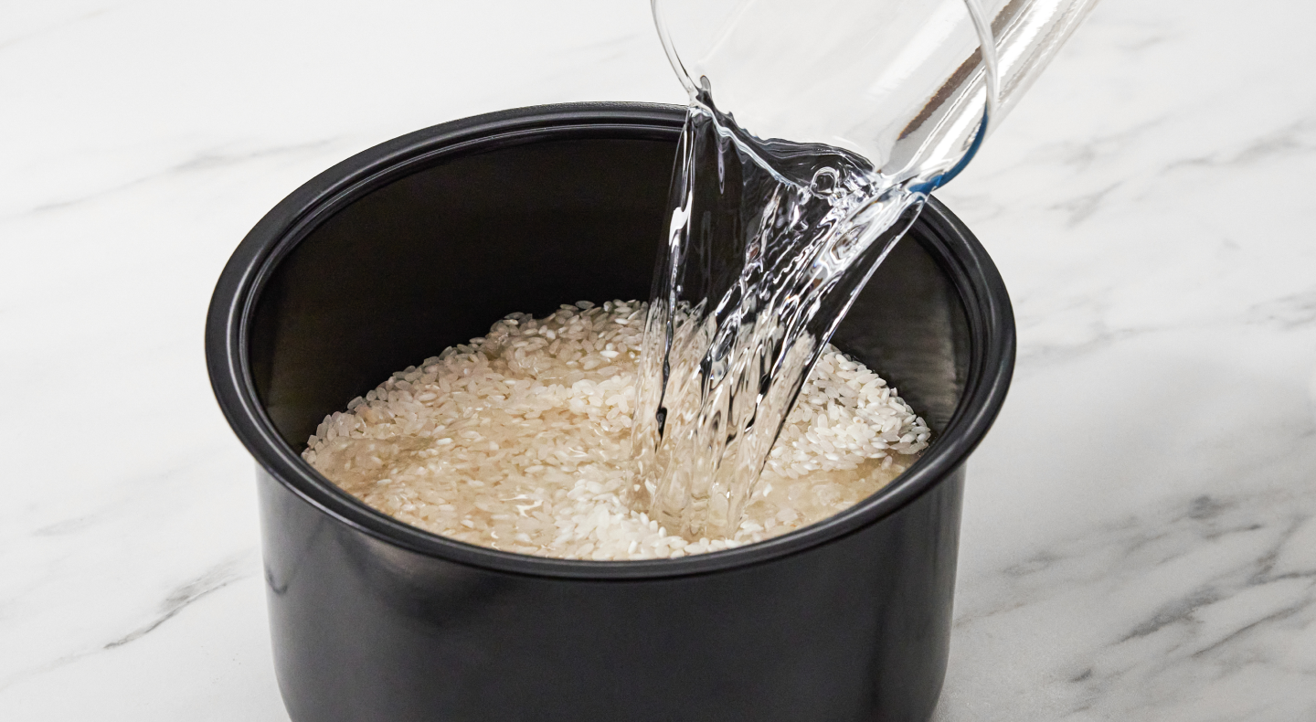 Water being poured into a grain and rice cooker filled with rice