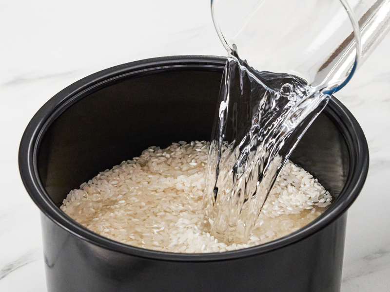 Water being poured into a grain and rice cooker filled with rice
