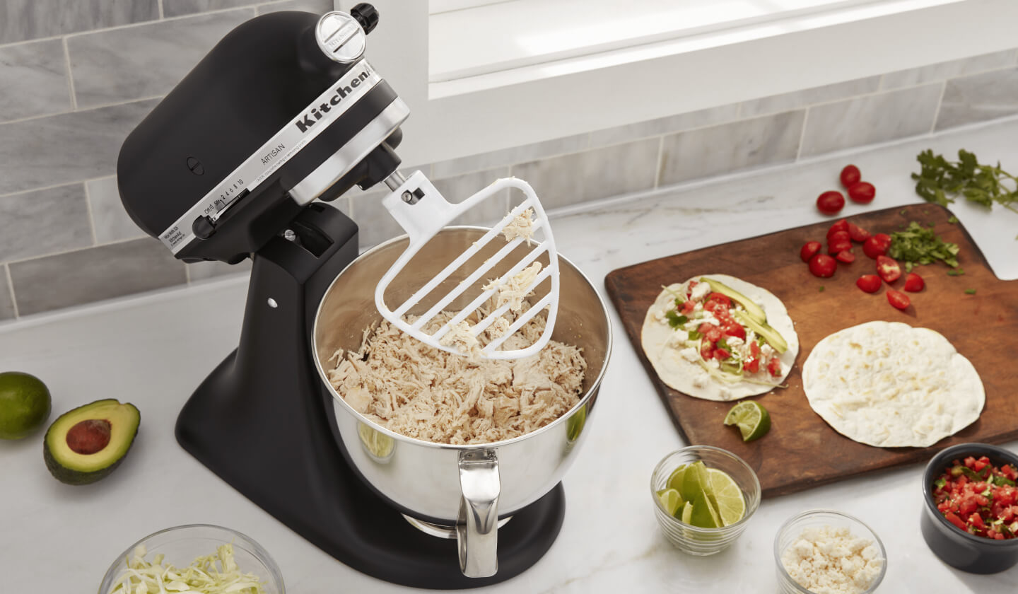 KitchenAid® stand mixer on a modern kitchen counter shredding cooked chicken.