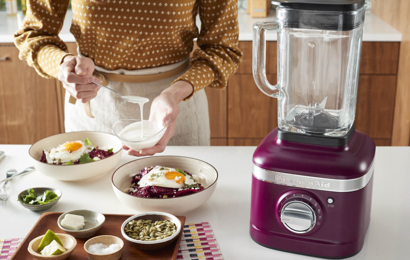 Woman preparing a meal next to a KitchenAid® blender. 
