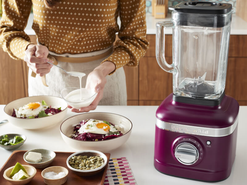 Woman preparing a meal next to a KitchenAid® blender. 
