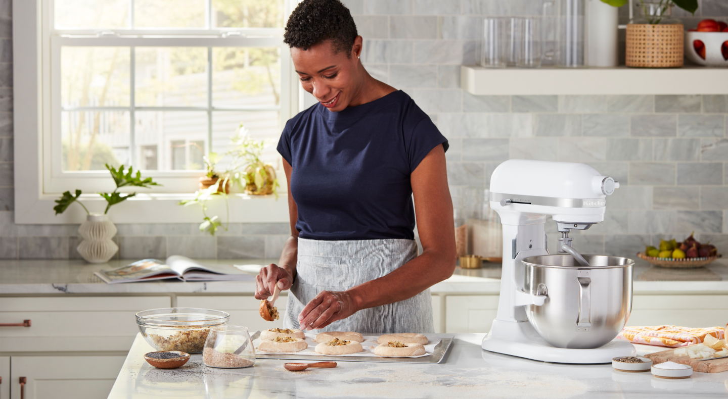 Person sprinkling herbs and seeds on top of shaped bagel dough