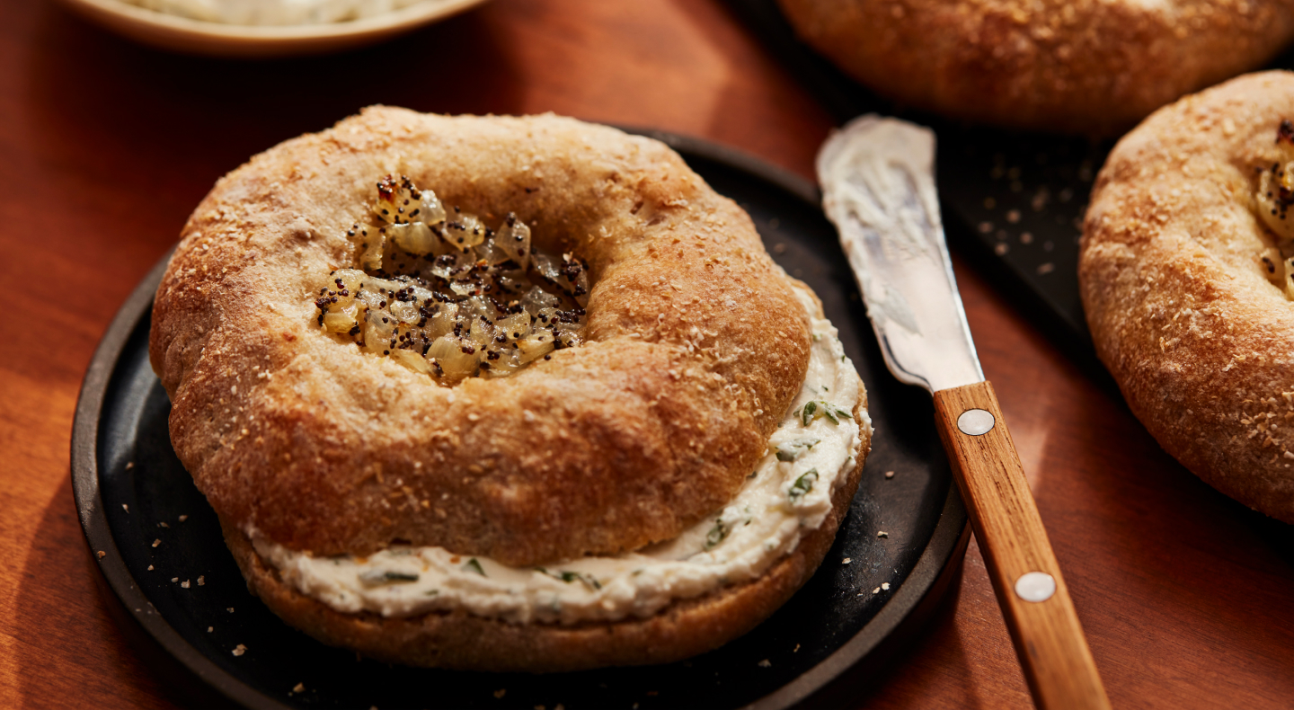 Prepared, spiced bagel with cream cheese inside, next to a spreading knife