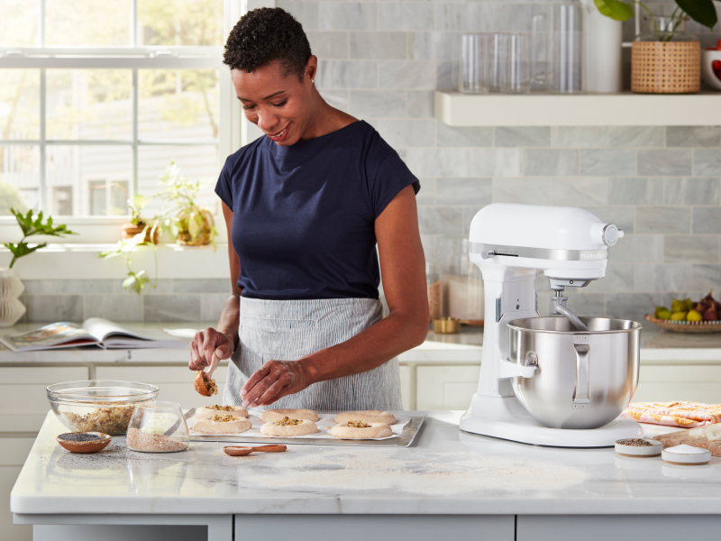Person sprinkling herbs and seeds on top of shaped bagel dough