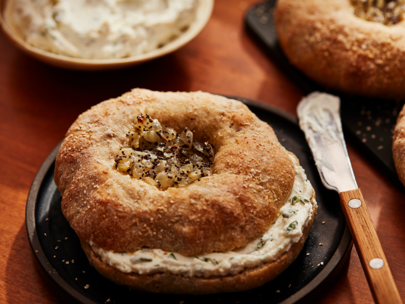 Prepared, spiced bagel with cream cheese inside, next to a spreading knife